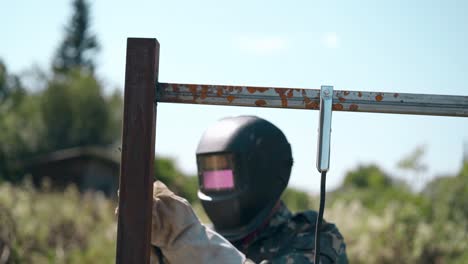 repairman in mask prepares fence parts for welding on day