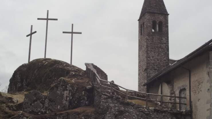 Kameraet vipper op mod en lille klippekirke med tre kors ved siden af, i en skov i de italienske Alper, 4K slow motion-detalje af klokketårn.