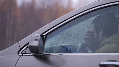 tired driver yawns, tries to stay awake and starts car, autumn rain daytime