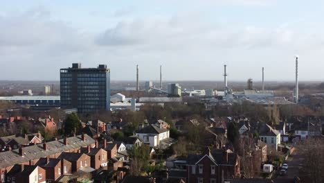 Aerial-view-over-park-trees-to-industrial-townscape-property-with-blue-skyscraper,-Merseyside,-England