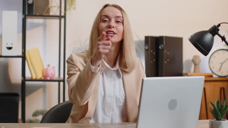 Business-woman-works-on-office-laptop-pointing-to-camera-looking-with-happy-expression-making-choice