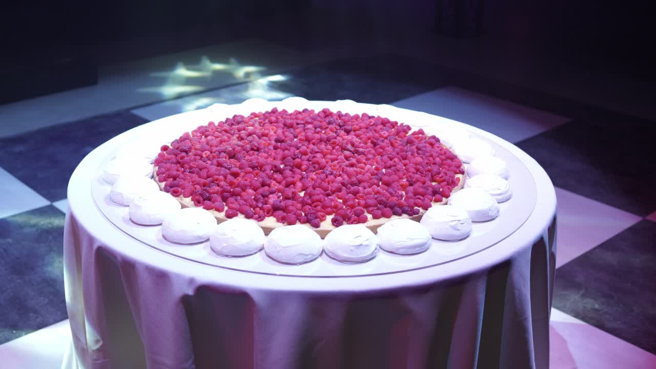 Close up of a large raspberry tart with meringue border displayed on a round table under soft lighting