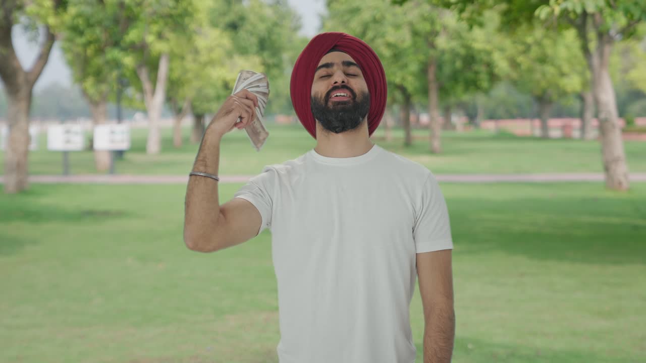 hombre indio sikh feliz usando dinero como ventilador en el parque