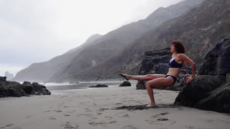 the ocean serves as a backdrop as a young, slender female athlete executes slow-motion push-ups on a rock