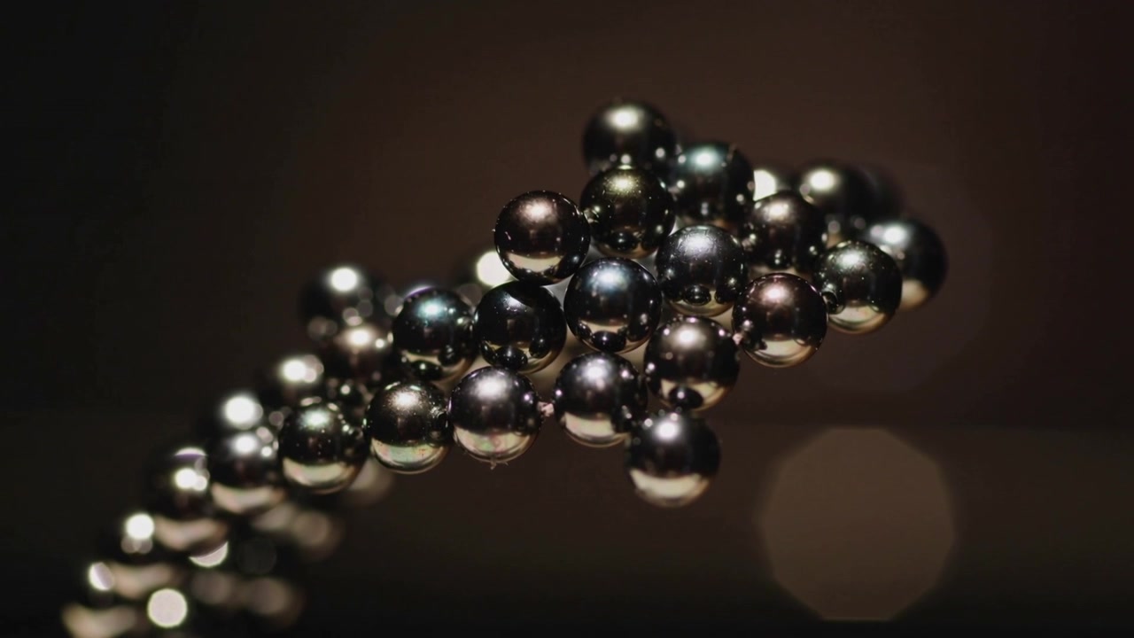 Un grappolo di sfere metalliche rotanti si avvicina in studio, mentre la telecamera si muove rivelando l'effetto bokeh e la lucentezza.