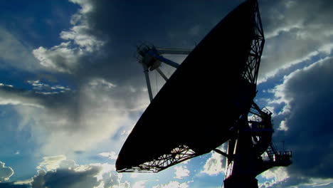 a satellite dish is moves and is silhouetted against the sky