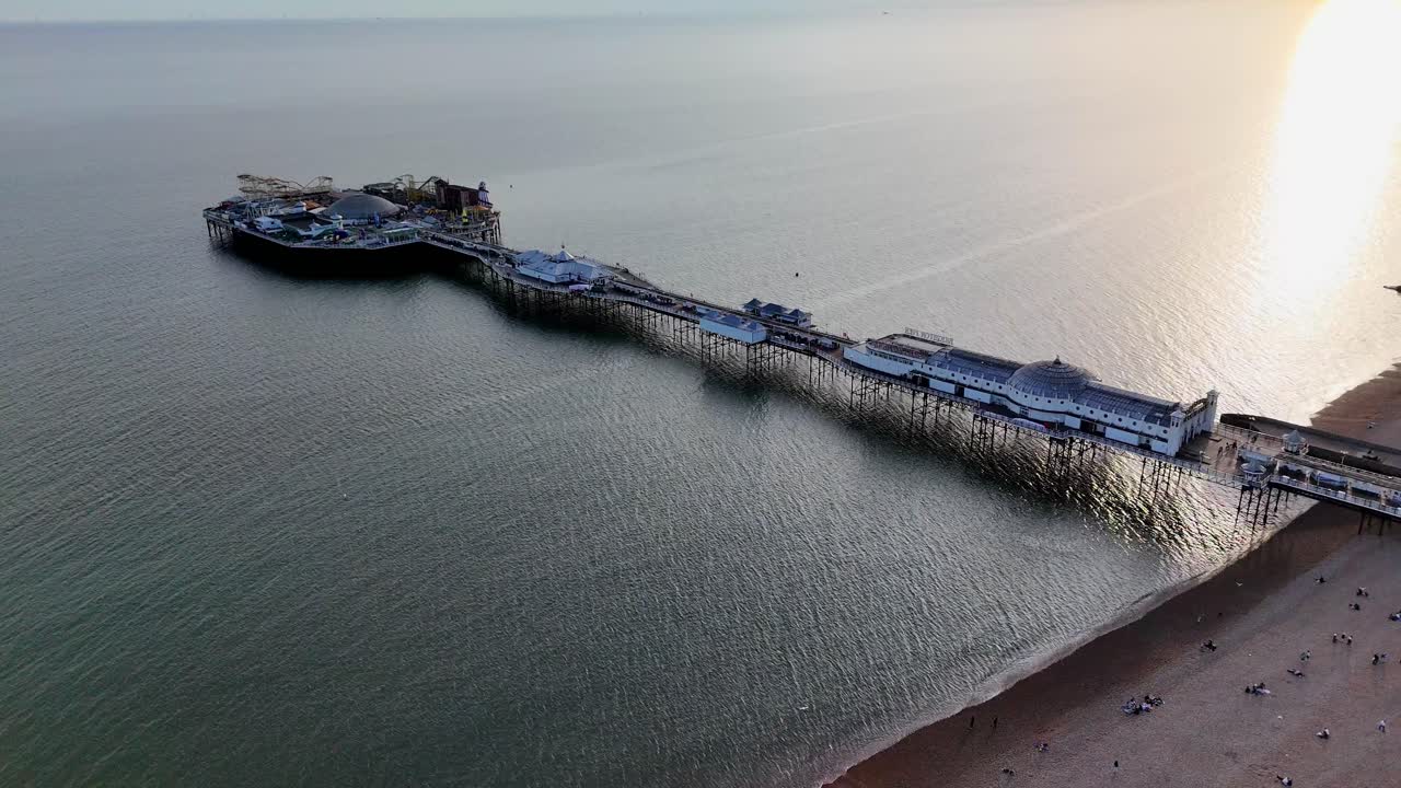 Stunning aerial drone footage of Brighton Palace Pier at sunset. Golden hour lights up the iconic seaside attraction, waves shimmer, and the sky glows in breathtaking colors.