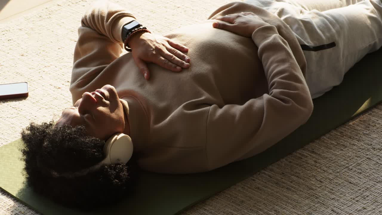 App audio starting in smartphone, woman lying on green mat practicing deep breathing to relax