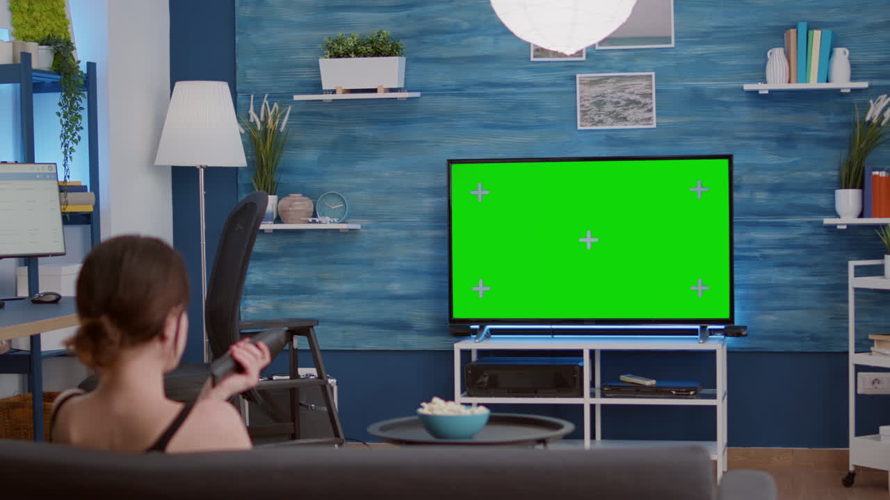 Young woman relaxing televison on green screen mockup display changing stations with remote control