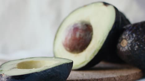 Eine-Avocado-Wird-In-Zwei-Hälften-Geschnitten-Und-Eine-Hälfte-Fällt-In-Zeitlupe-Auf-Den-Tisch,-Wodurch-Das-Innere-Und-Der-Kern-Freigelegt-Werden