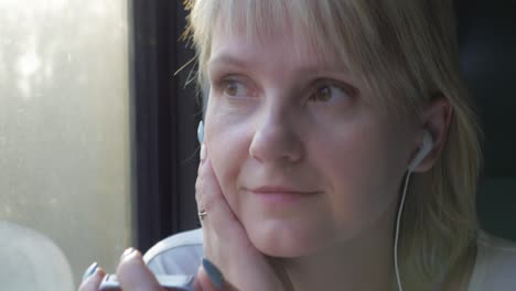 joven mujer caucásica viaja en un compartimento de tren, se sienta junto a la ventana, escucha música en auriculares