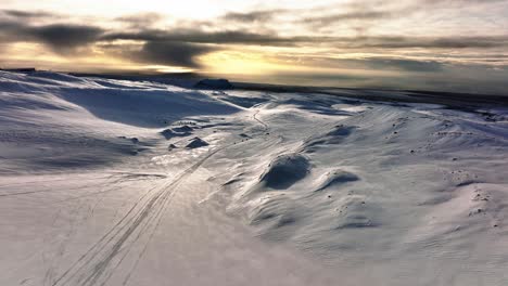 Aerial-landscape-view-of-people-riding-snowmobiles-on-Myrdalsjokull-glacier-in-Iceland,-during-an-epic-sunset