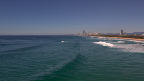 aerial view of drone tracking a wave as it breaks on a beautiful day with the city of surface paradise in the background at the popular seaway lookout the spit gold coast qld australia