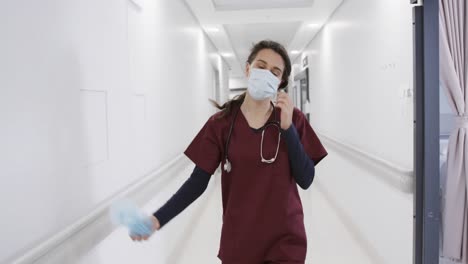 Doctora-Caucásica-Quitándose-La-Mascarilla-Y-La-Gorra-Caminando-En-El-Pasillo-Del-Hospital,-Cámara-Lenta