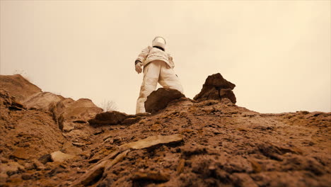 An-astronaut-wearing-a-spacesuit,-moving-across-a-deserted-planet-with-red-soil,-looks-off-into-the-distance