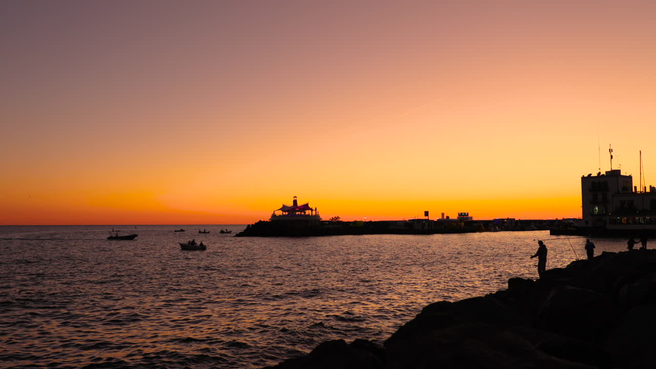 silueta de pescador en la costa pedregosa durante la puesta de sol naranja lanzando sedal en mar abierto en el fondo es la ciudad y el puerto de la puesta del sol gran valle de la isla canaria 4k captura en cámara lenta a 60fps