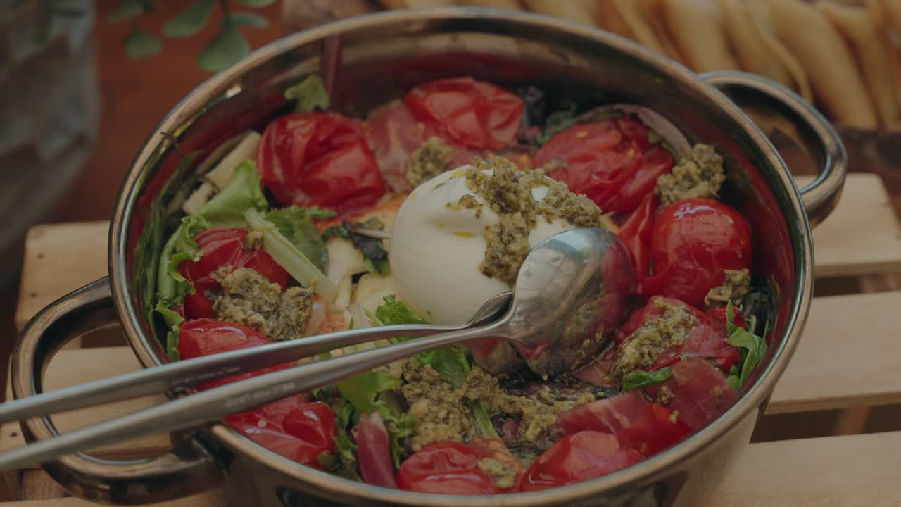 Fresh burrata cheese salad with roasted cherry tomatoes, pesto, and greens served in rustic bowl