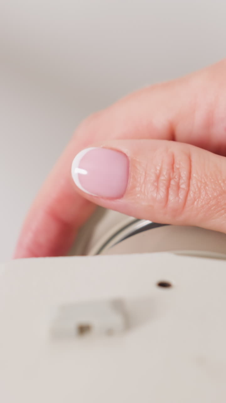 closeup manicured nails adjusting small dial on machine, pink polish visible as fingertip rotates tension ring, gentle tactile motion, studio lighting emphasizes smooth texture, meticulous calibration