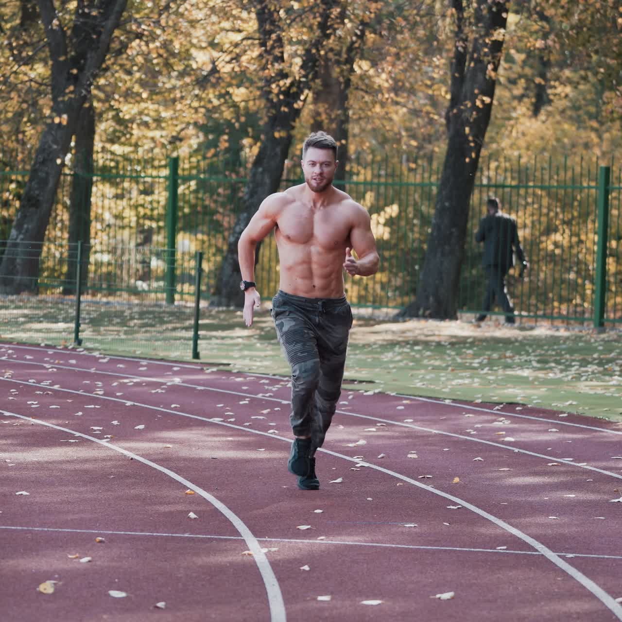 Fitness young man running at sports stadium. Shirtless sportsman running outside on athletics track in autumn. Healthy lifestyle.