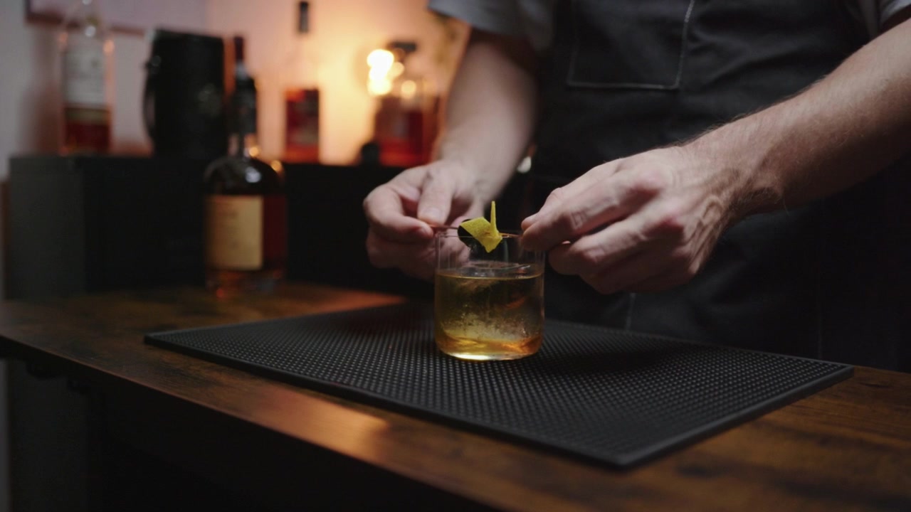 Cocktailpynt. Bartender færdiggør en klassisk cocktail med et kirsebær og citron. Dygtig bartender laver en cocktail i en hjemmebar. Perfekt til mixologi-tutorials eller livsstils-vlogs