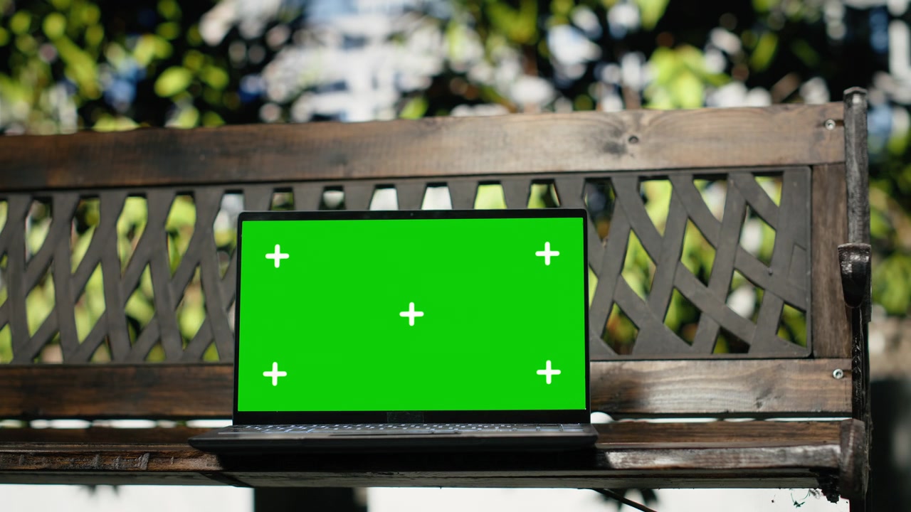 Mockup di laptop con schermo verde su una panchina di legno vuota in un parco cittadino.
