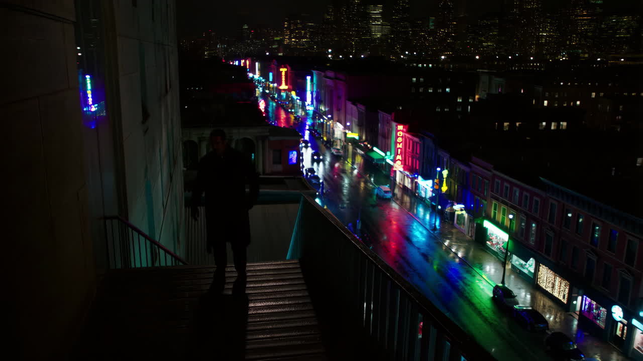 A lone figure overlooks a vibrant, neon-lit city street at night