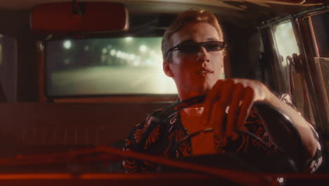 young man in retro car enjoying night drive through city