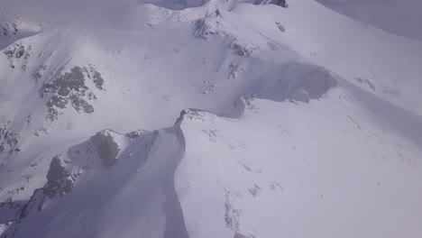 Vista-Aérea-De-La-Cresta-De-La-Montaña-Cubierta-Por-Un-Manto-De-Nieve-Blanca