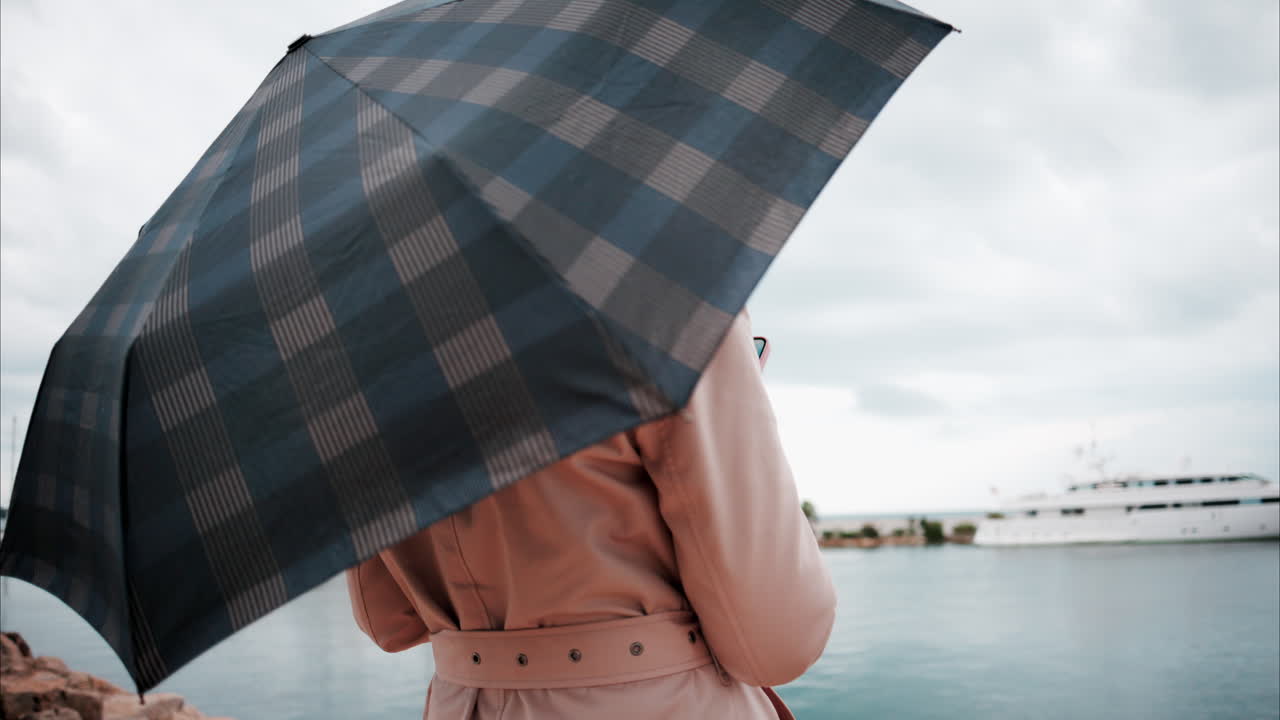 Woman wearing a trench coat looking at the sea in the rain in Cannes, France