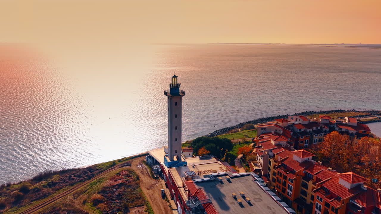 Quartiere residenziale di case colorate e faro situato sulla costa. Un sole splendente illumina il paesaggio marino sullo sfondo. Prospettiva aerea