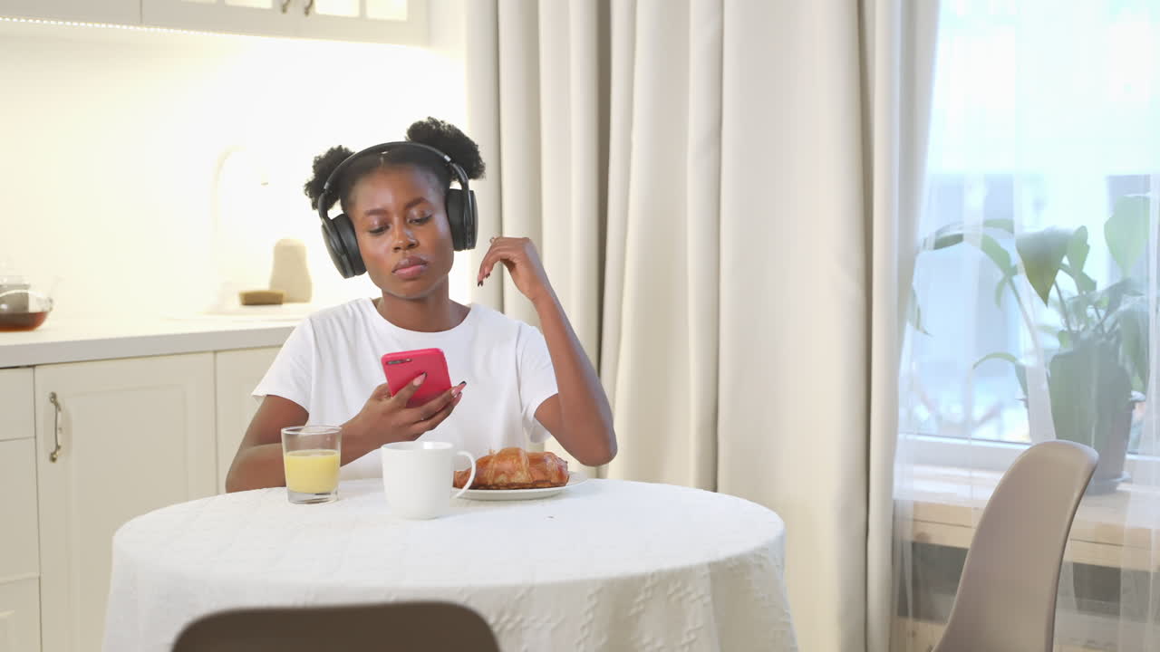 mujer tomando el desayuno mientras usa un teléfono y escucha música en la cocina.