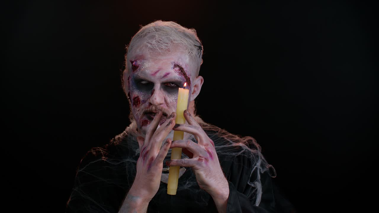 hombre siniestro con horrible aterrador halloween maquillaje zombi haciendo caras, hechizos conjuros sobre una vela