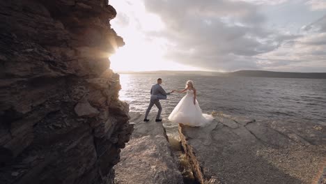 groom goes to bride and gives her a hand. newlyweds on mountainside by the sea