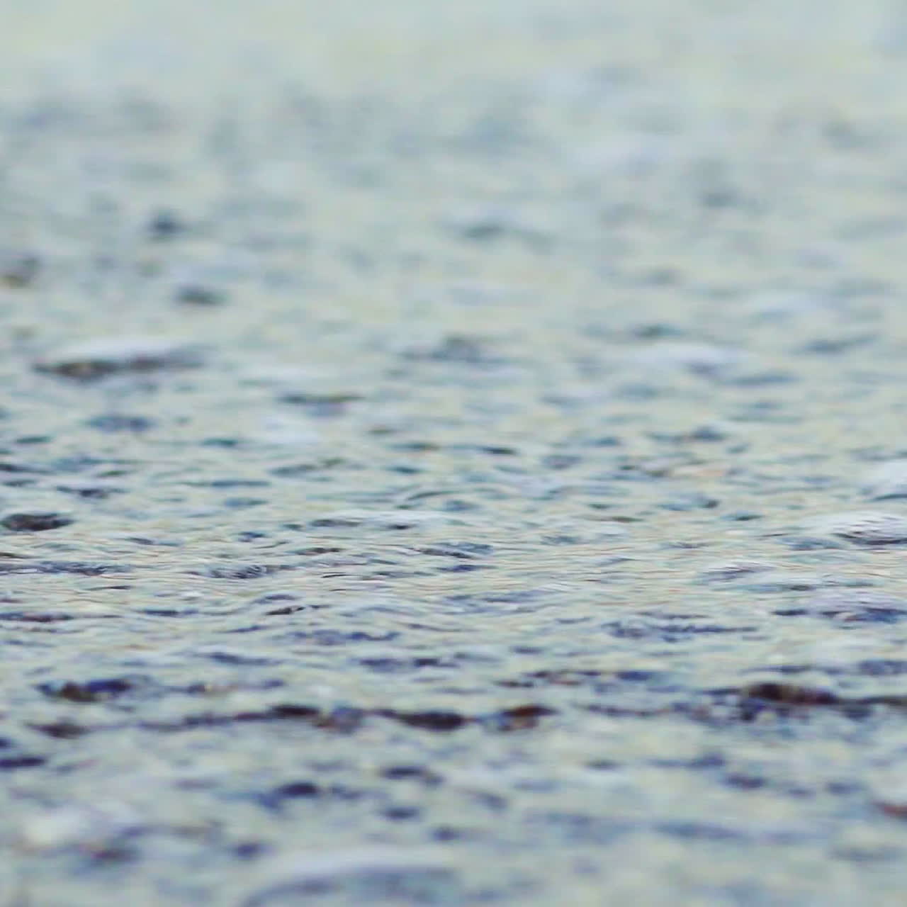 Natural view of water waves covering the shore with little colorful rocks at the sea. Sea marine with white foam on a beach. Close-up