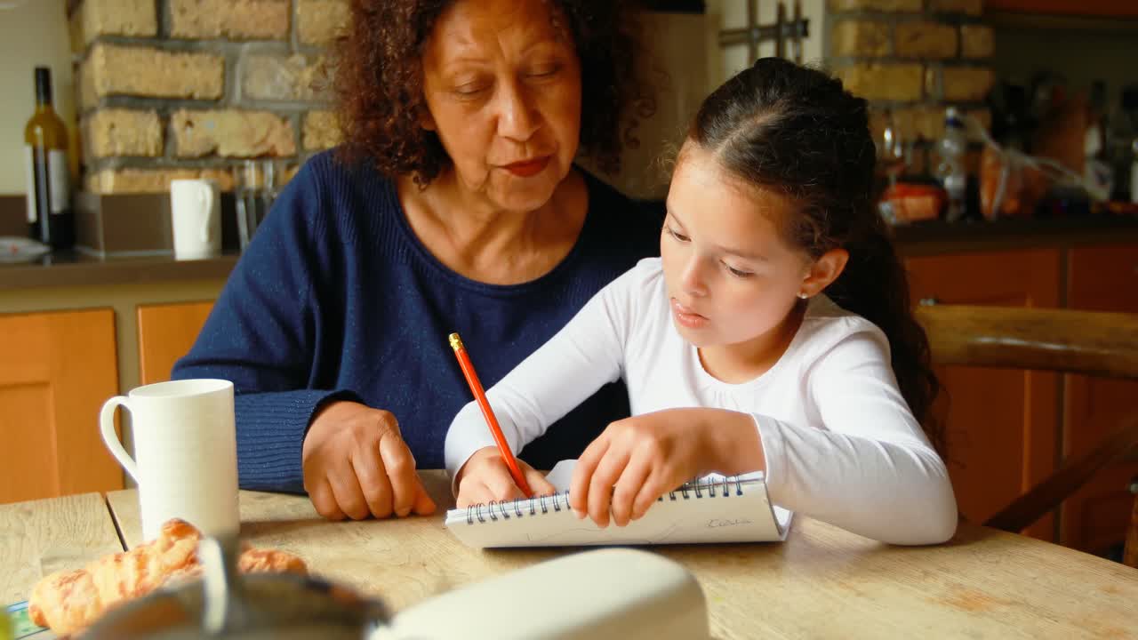 chica escribiendo en el bloc de notas con su abuela en la cocina 4k