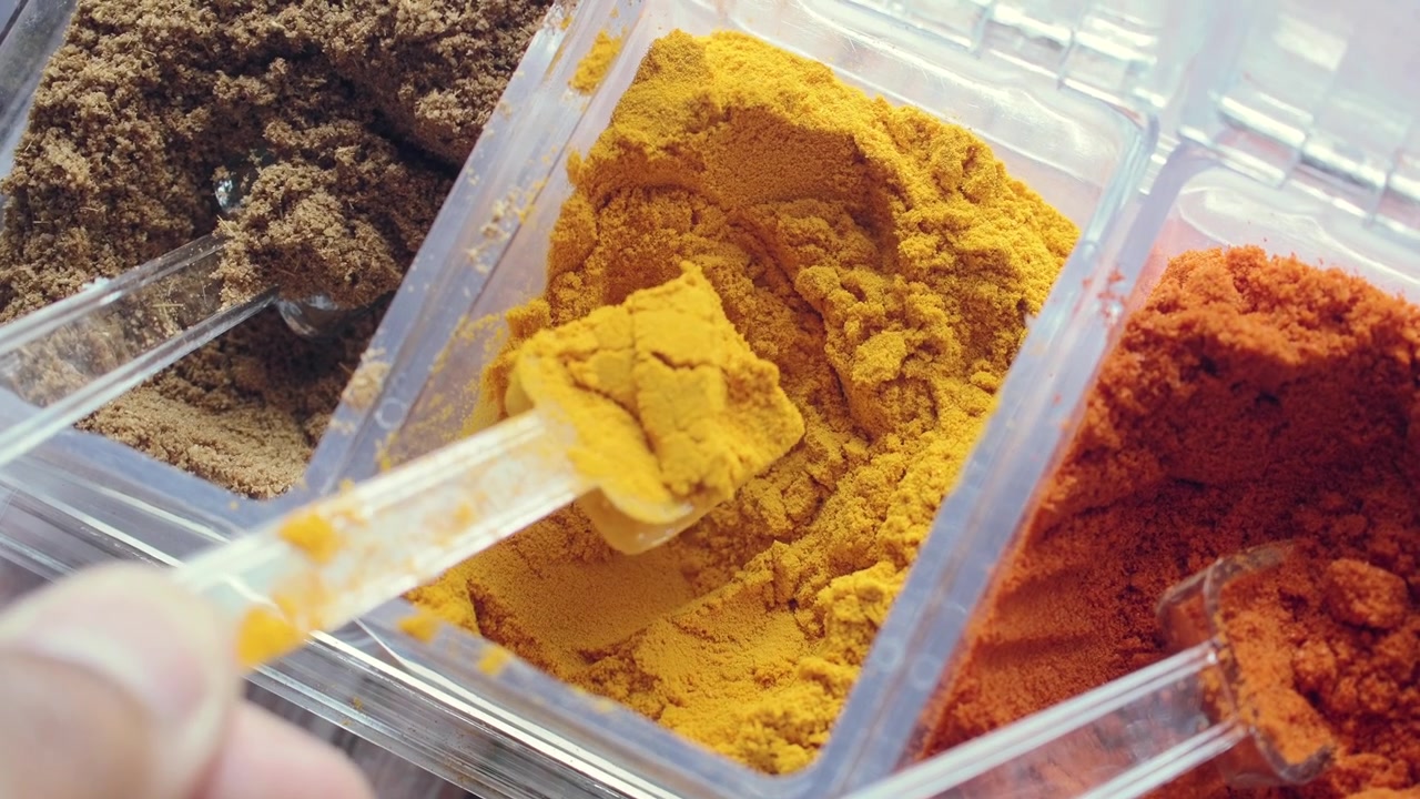 Hand Scooping Vibrant Yellow Turmeric Powder from a Container