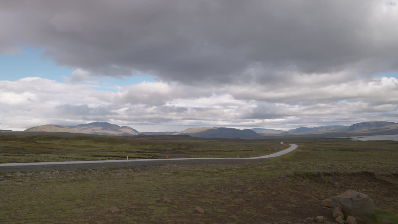 A car drives along the long desolate highway to Thingvellir National Park in Iceland, epic landscape