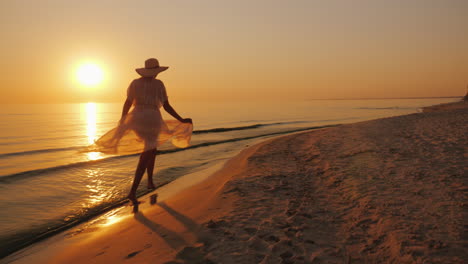 Eine-Frau-In-Einem-Leichten-Paar-Spaziert-Bei-Sonnenuntergang-Am-Strand-Entlang-Sorglose-Und-Fröhliche-Frau