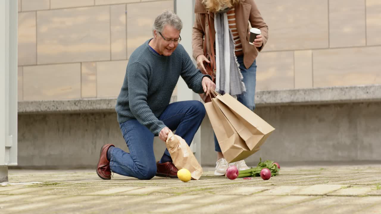 Couple walking plaza balancing bags on step and coffee spilling produce retrieving items