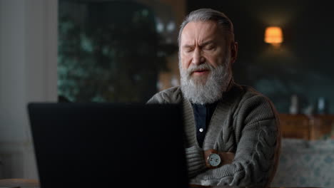 strict old man talking during video call on laptop in vintage home room