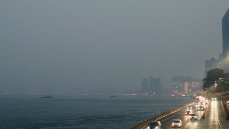 Ciudad-De-Nueva-York-Cubierta-De-Humo-De-Incendios-Forestales-Con-Tráfico-A-Lo-Largo-De-Fdr-Drive,-La-Cámara-Gira-Y-Gira-Hacia-Abajo-Para-Revelar-La-Isla-Rosevelt-Mientras-Un-Ferry-Cruza-El-Marco-Y-La-Cámara-Retrocede-Hacia-La-Pasarela-Peatonal