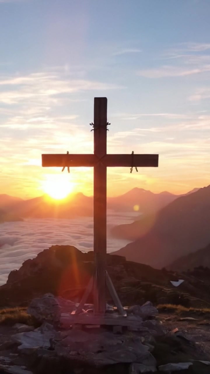 Maestosa silhouette di croce di legno contro un'alba vibrante sulle cime delle montagne e sulla valle, che celebra la natura e la riflessione spirituale.