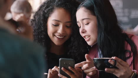 happy teenage girl friends using smartphones drinking coffee in cafe texting hanging out sharing gossip enjoying chatting together