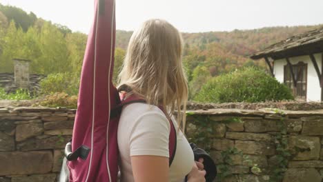 músico femenino admira la vista de otoño camina por la calle amurallada aldea rústica