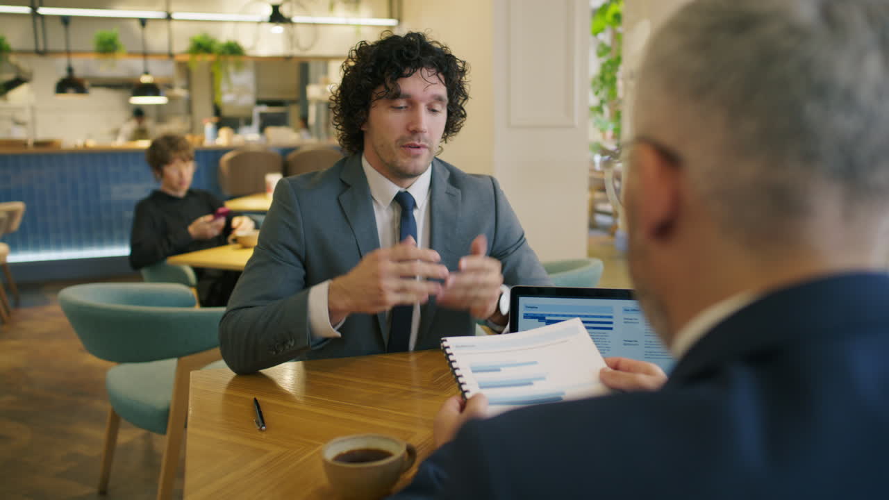 Businessman Explaining Financial Report to Colleague at Meeting in Cafe