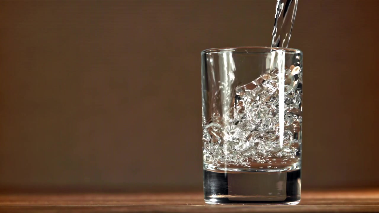 Klar væske hældes i et glas i slowmotion