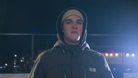 hombre con capucha sosteniendo una pelota bajo la brillante luz de la calle, profundamente en pensamiento durante la noche, transmitiendo introspección y profundidad emocional, fondo urbano iluminado por las luces de la ciudad