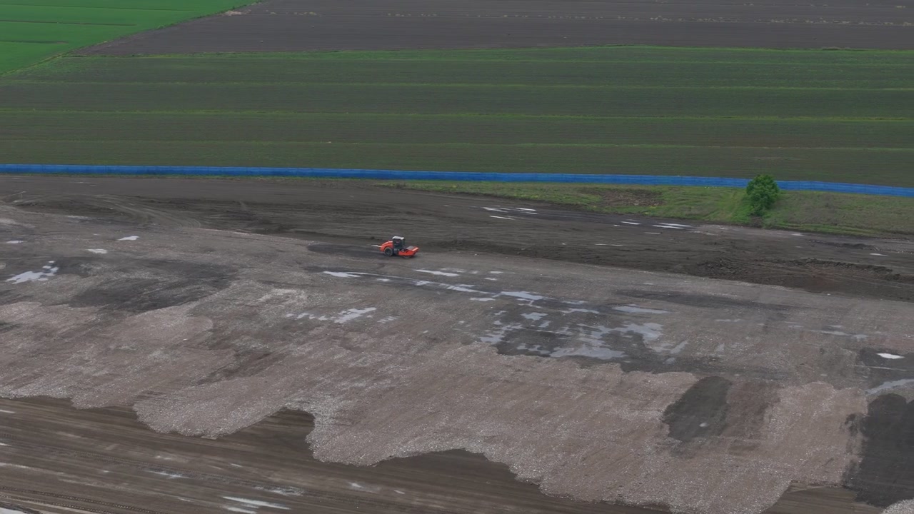 Bulldozer cingolato che livella un cantiere per un polo logistico vicino a Fiorenzuola d'Arda, Piacenza, Emilia-Romagna, Italia, rivelando piazzole di costruzione livellate, movimento terra e terreni agricoli circostanti, ripresa drone