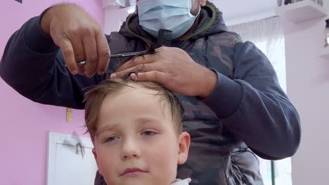 Young-boy-getting-haircut-in-barbershop,-closeup-view-of-face-and-scissors,-covid-time