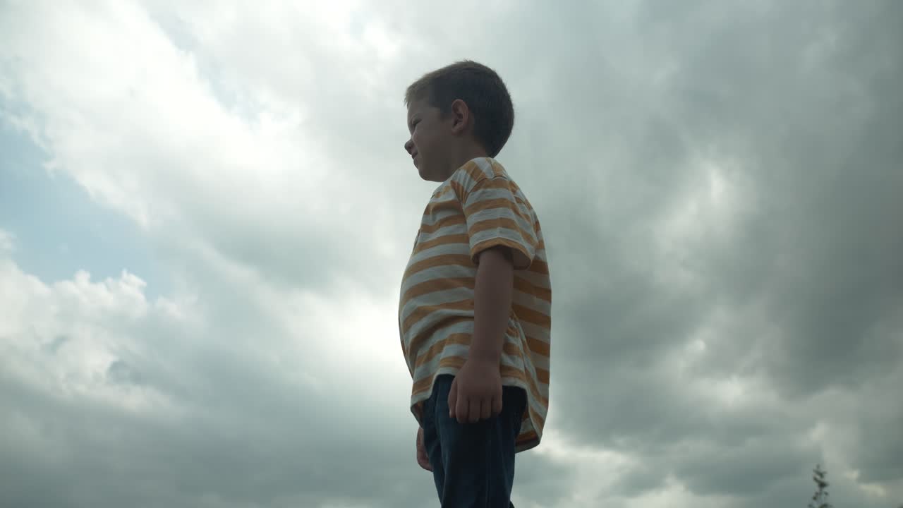 A young boy looking up at the sky in slow motion, his eyes full of wonder and curiosity. This cinematic footage captures the innocence and imagination of childhood.